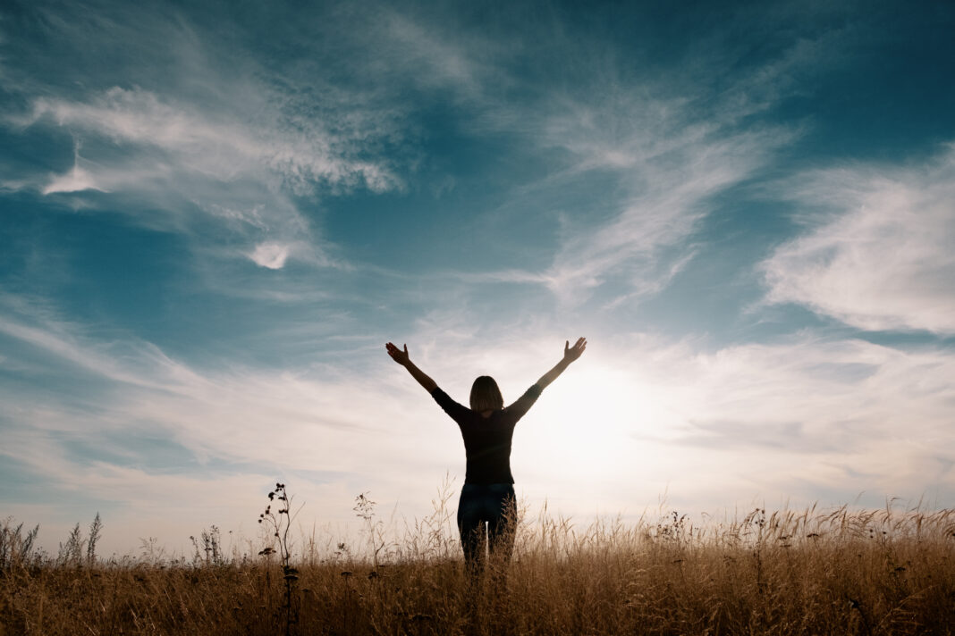 Young happy woman in a golden field on sunset.