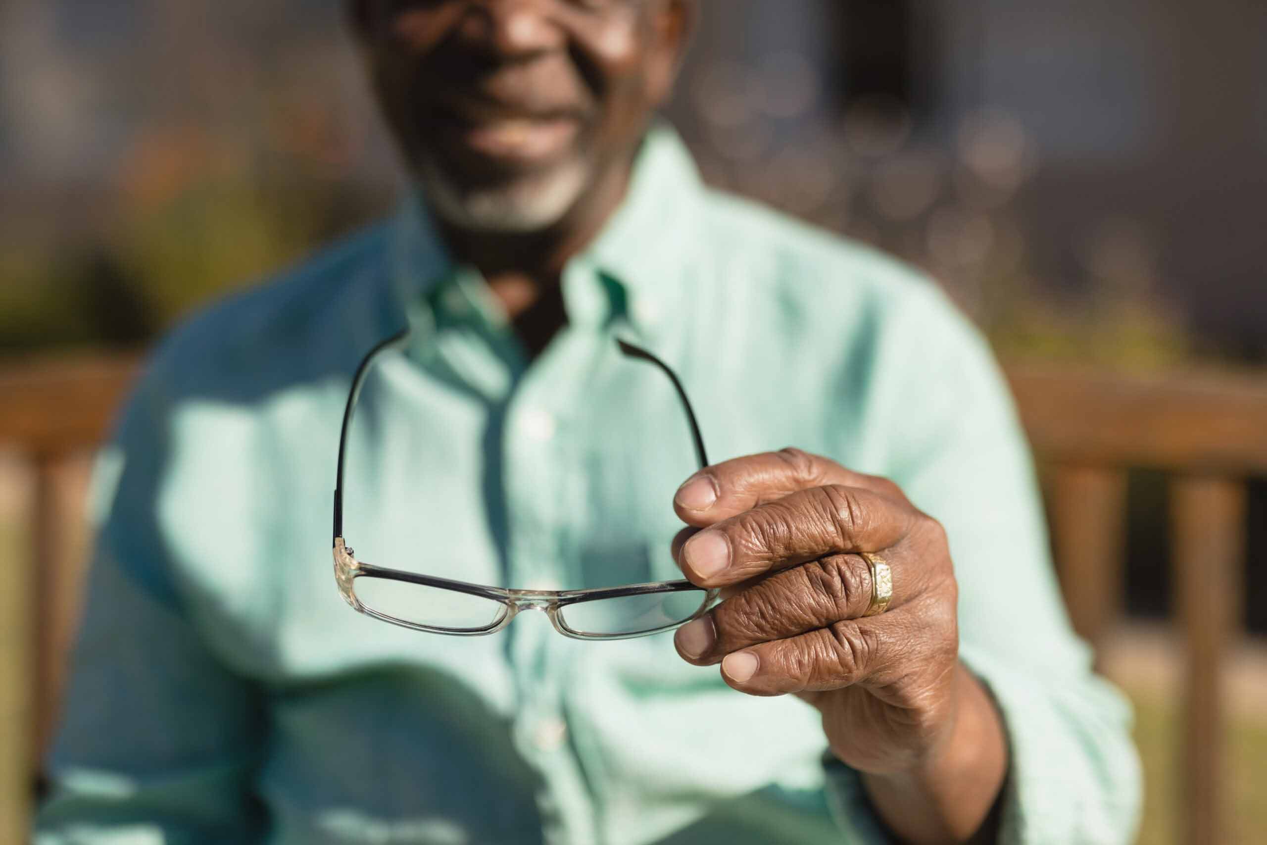 Mid section of senior African-American man holding spectacle in the park of nursing home