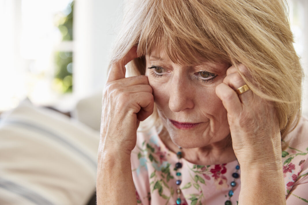 Senior Woman Sitting On Sofa At Home Suffering From Depression